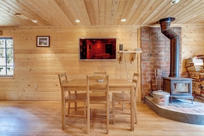 Un interior de madera con una mesa de comedor, sillas, una chimenea y un televisor montado en la pared.