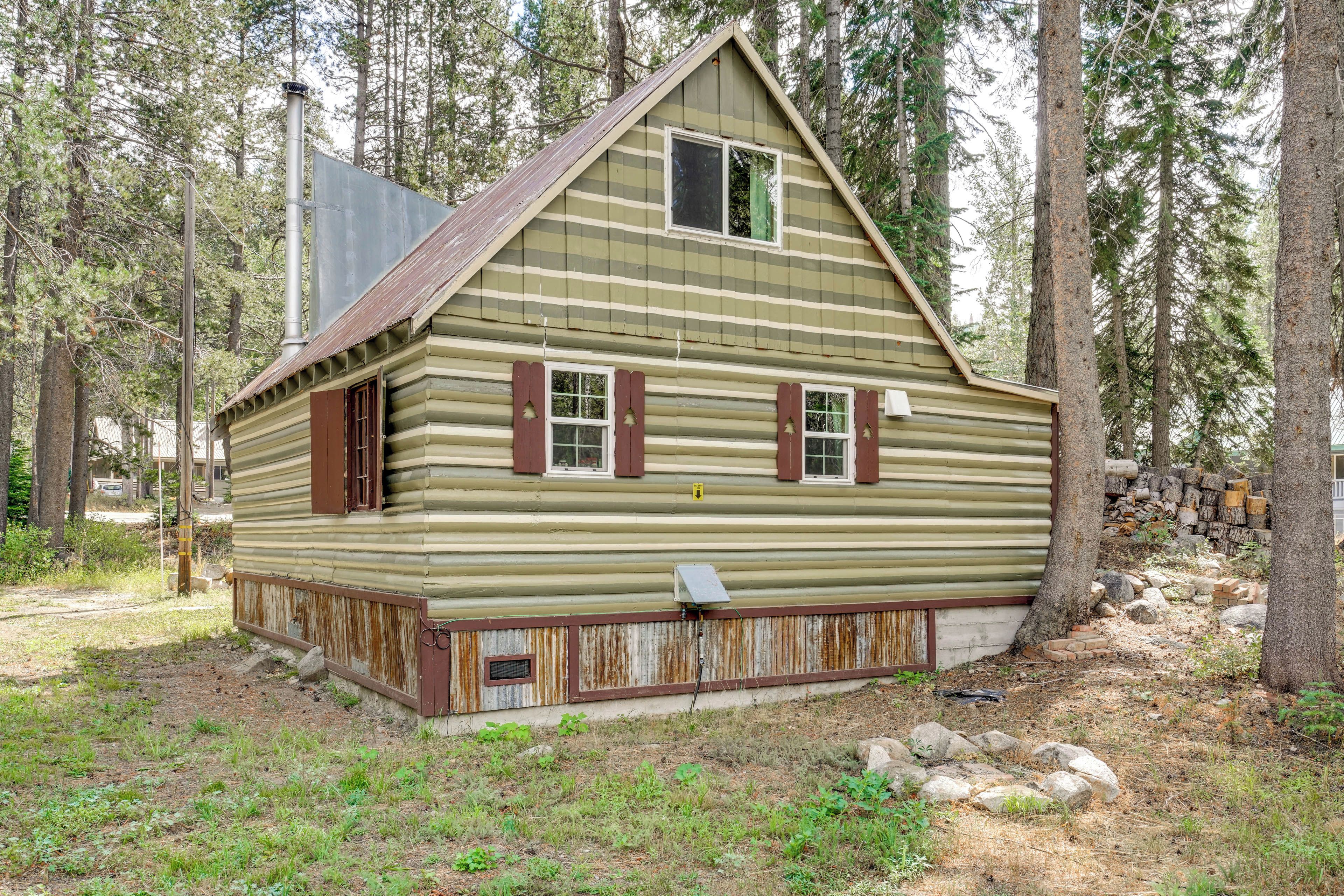 A rustic log cabin with a steep gabled roof, a small front porch, and a chimney.