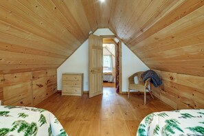 Un dormitorio acogedor en el ático con paredes de madera, una cama individual, un aparador y una silla.