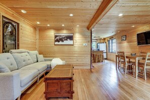 Ein gemütliches Blockhaus-Interieur mit einer Couch, einem Esstisch, Stühlen, Holzwänden und einem Bärenbild.