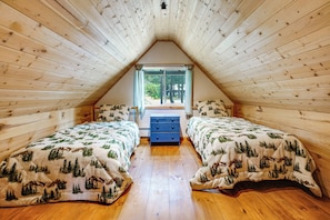 A cozy attic bedroom with two beds, a dresser, and a window with a view of trees. - Cozy Mountain Cabin Skiing Hiking Biking Swimming (Truckee)