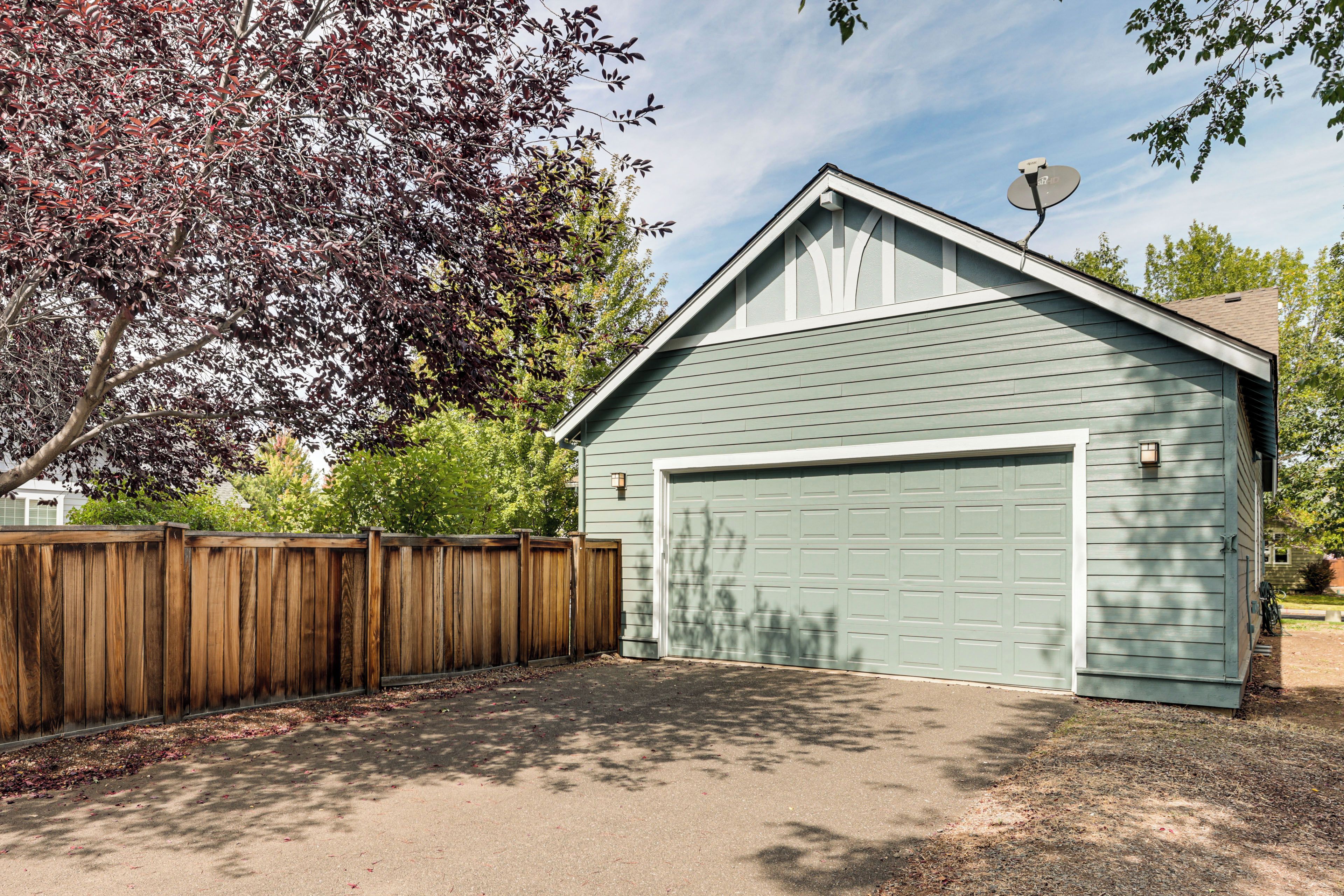 A single-story building with a garage, a wooden fence, and a satellite dish.