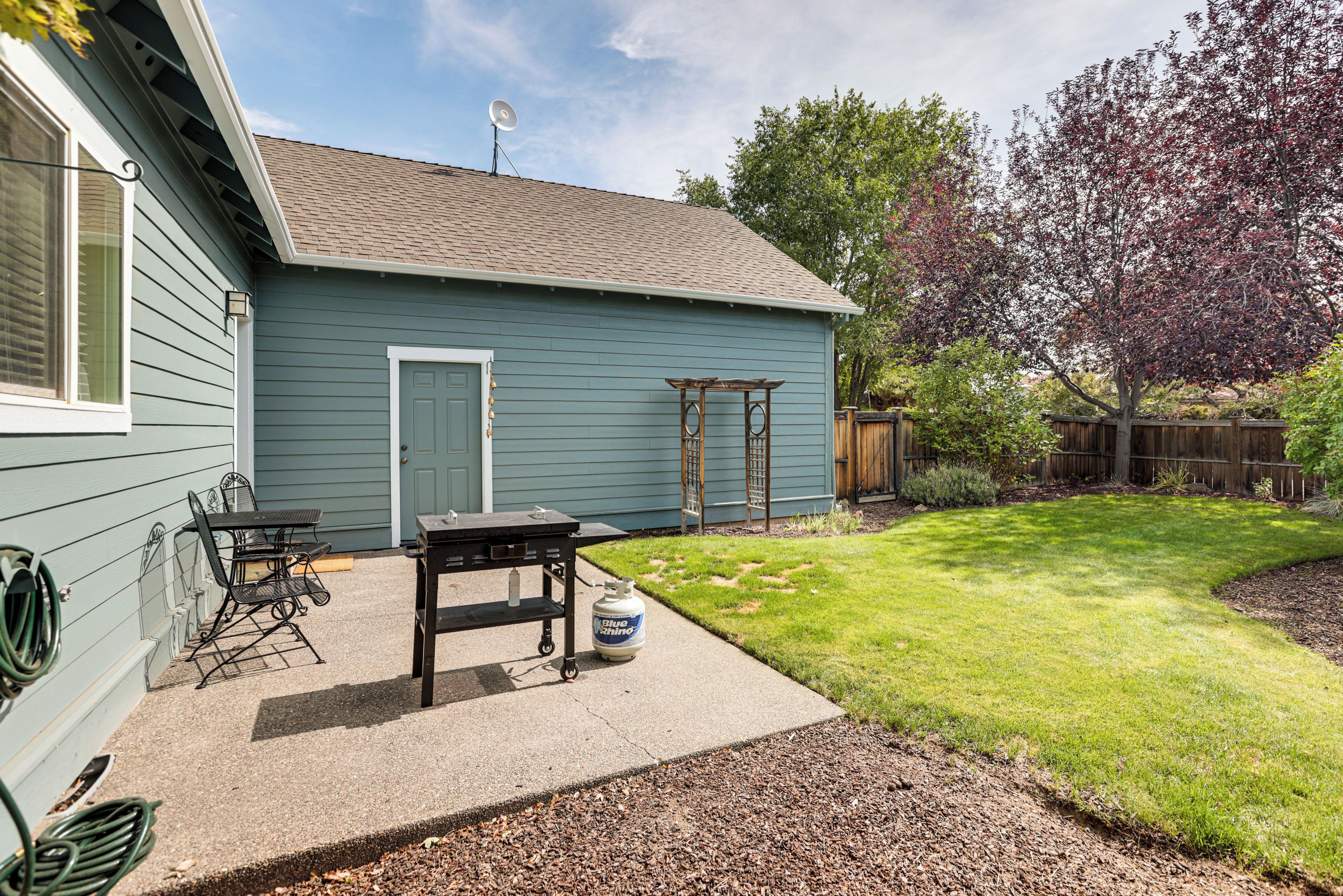 A residential backyard with a patio area, a barbecue grill, and a propane tank.