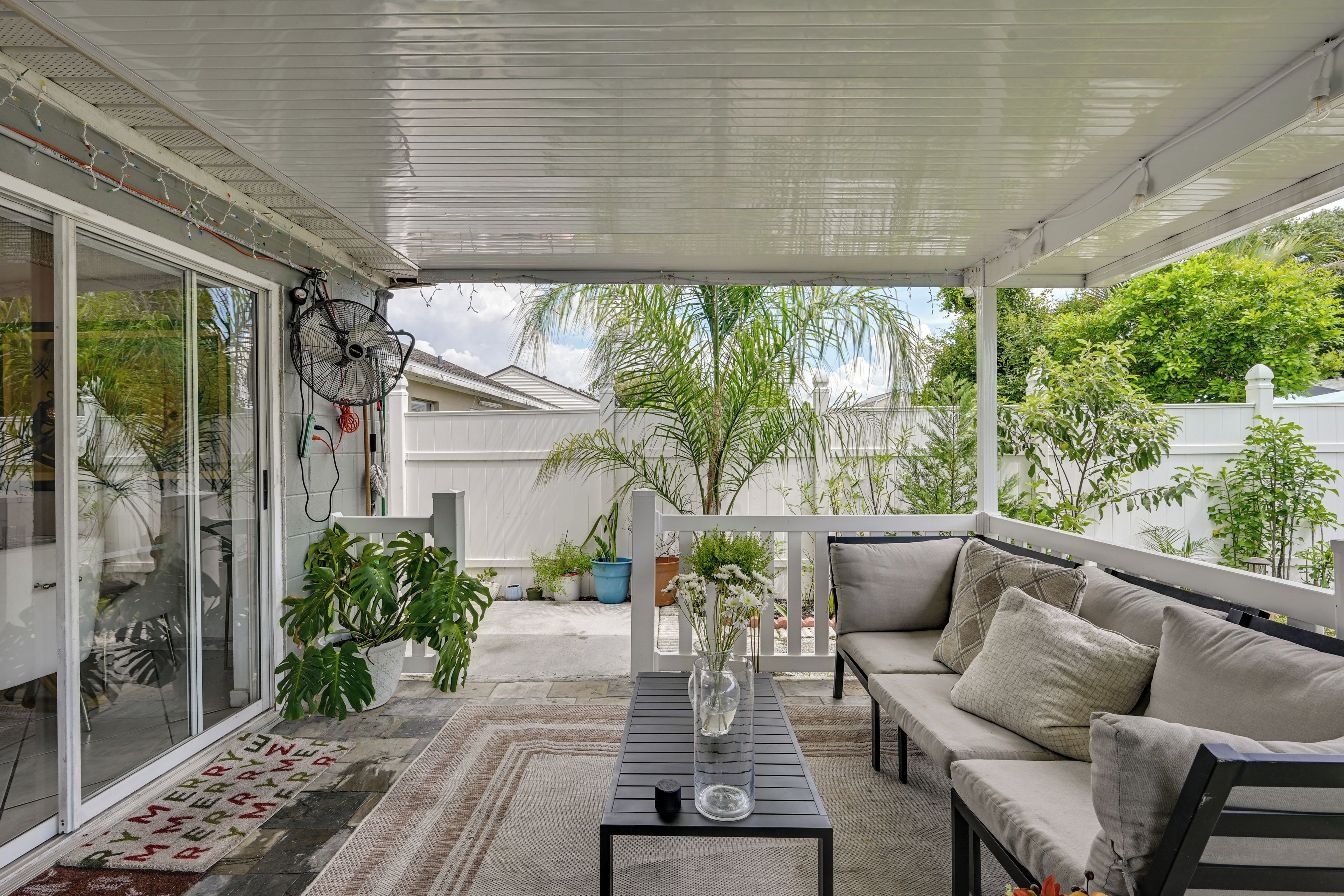 A covered outdoor seating area with a sofa and a table, surrounded by potted plants and a view of the neighborhood.