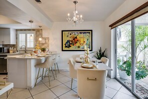 A modern kitchen with a dining area, featuring a chandelier, a large window with a view of greenery, and a contemporary painting on the wall. - Families w/ Pets! Home 10 Mi to Busch Gardens (Tampa)