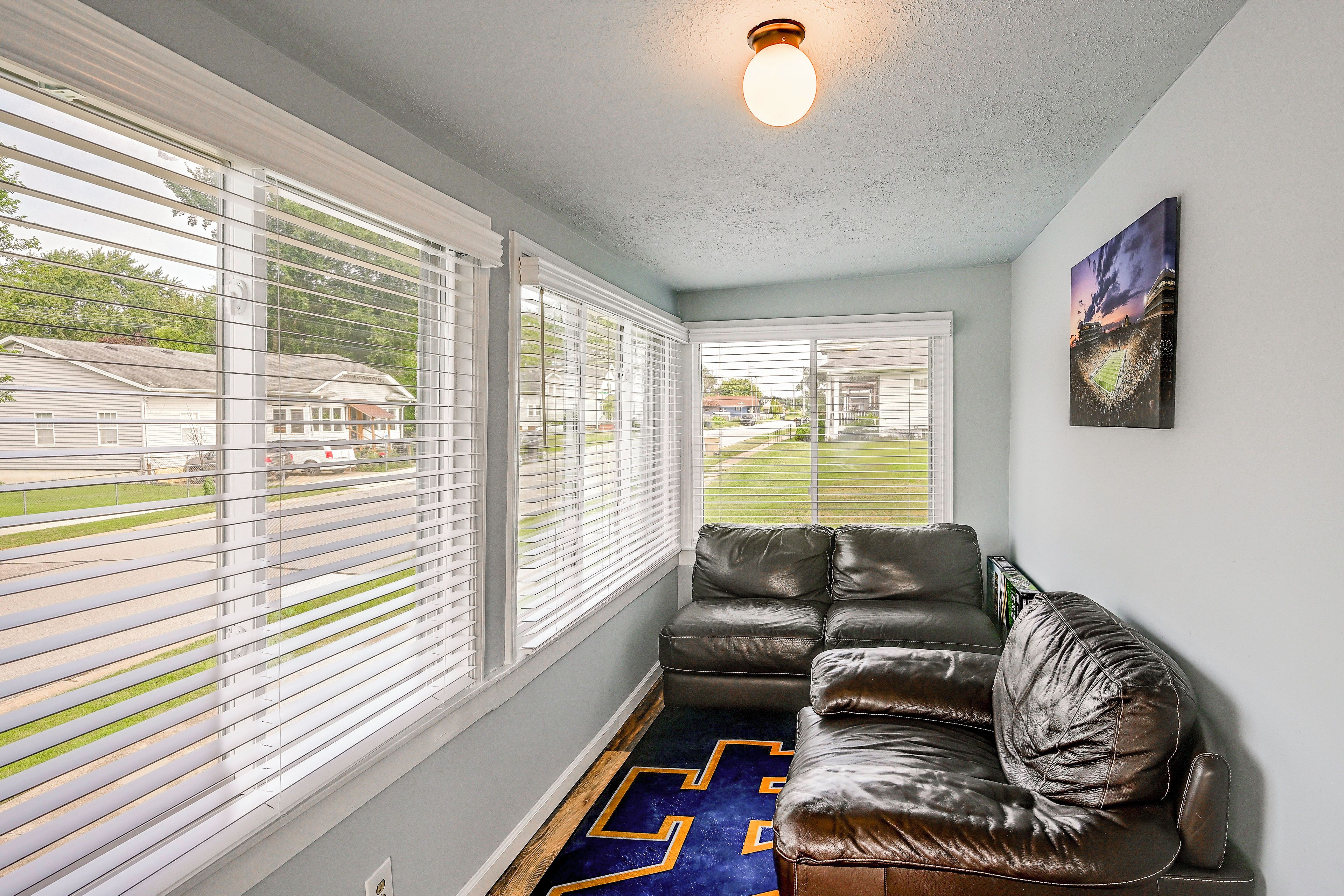A room with a leather sofa, large windows with blinds, a ceiling light, and a sports field view.