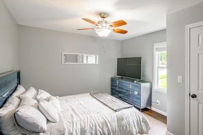 Quarto com cama, penteadeira, ventoinha no teto, espelho e televisão.
