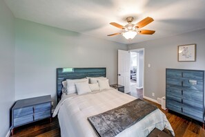 A bedroom with a bed, nightstands, a ceiling fan, a dresser, and a door leading to another room.