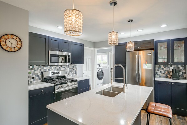 A modern kitchen with dark cabinetry, a central island, stainless steel appliances, and pendant lighting.