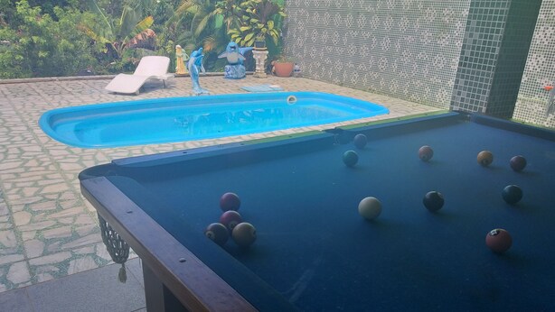 Une table de billard avec des billes et une autre table de billard dans un jardin, avec une terrasse carrelée et une piscine.