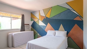 Une chambre d’hôtel avec un lit, une fenêtre avec des rideaux et un mur orné d’un motif géométrique.