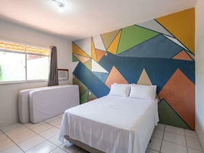 Una habitación de hotel con una cama, un ventanal con cortinas y una pared con estampado geométrico.