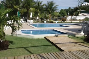 A swimming pool with a wooden deck, surrounded by palm trees and a fenced area.