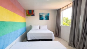 Une chambre avec deux lits, un mur aux couleurs vives, un tableau et une fenêtre avec des rideaux.