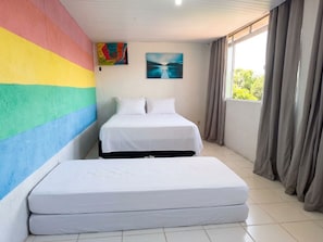 Una habitación con dos camas, un muro colorido, un cuadro y una ventana con cortinas.