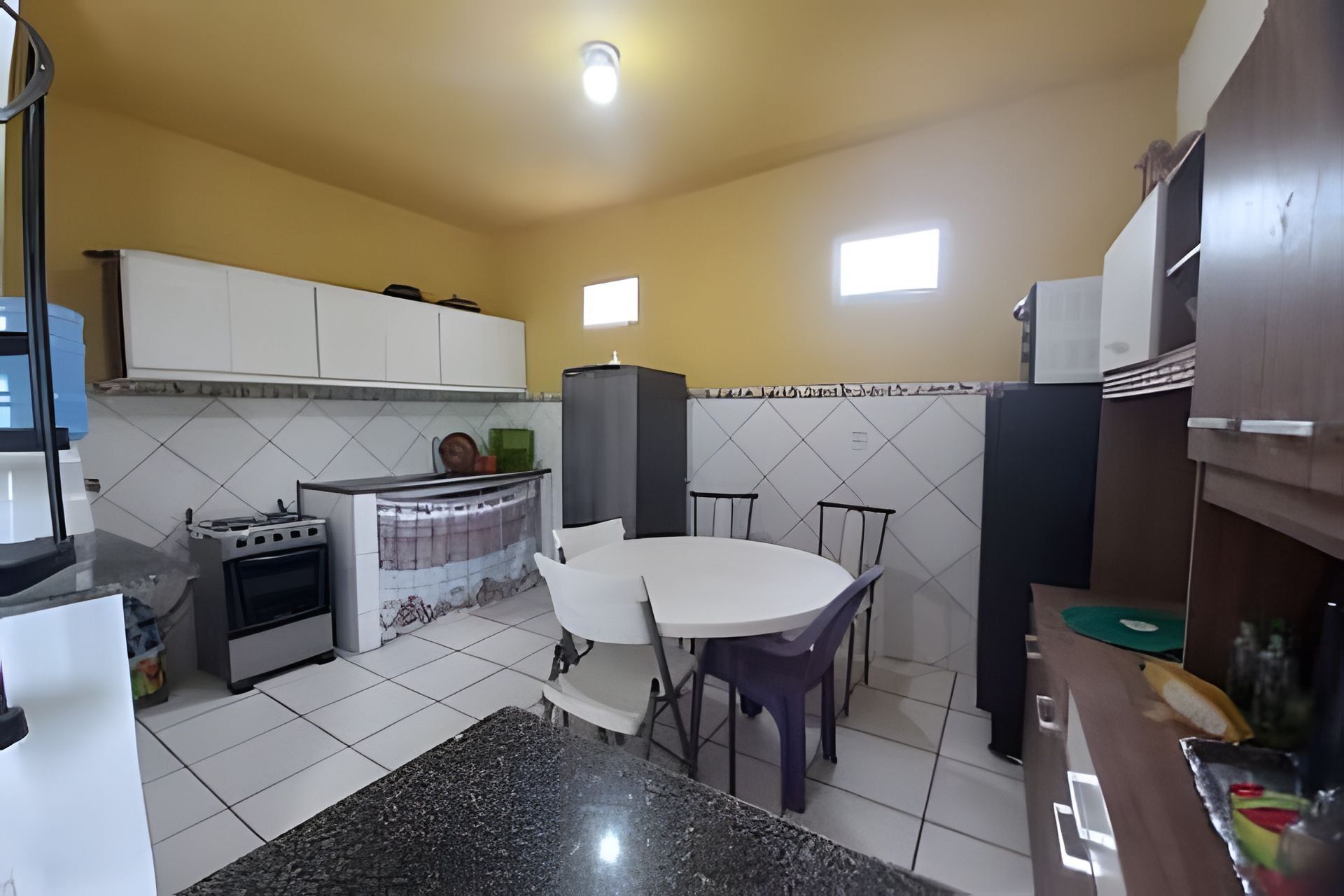 Uma cozinha com armários brancos, fogão, pia e mesa de jantar com cadeiras.
