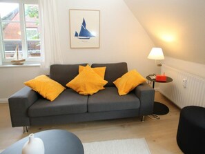 Un salon moderne avec un canapé gris, trois coussins jaunes, un vase blanc, une lampe et un tableau encadré au mur.