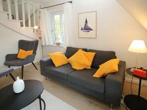 Un salon moderne avec un canapé gris, des coussins jaunes, un vase blanc et un tableau encadré représentant un voilier.