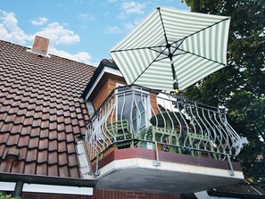 A balcony with a green and white striped umbrella, a tiled roof, and a metal railing. - Luttmarsch 13, Holiday Apartment 10 (Wyk auf Foehr)