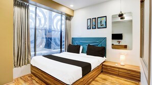 A hotel room with a large bed, a window with curtains, a headboard, a bedside table with a lamp, and wall-mounted artwork. - Collection O Vesu Surat (Surat)