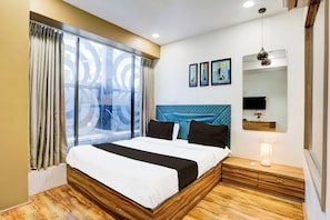 A hotel room with a large bed, a window with curtains, a headboard, a bedside table with a lamp, and wall-mounted artwork. - Collection O Vesu Surat (Surat)