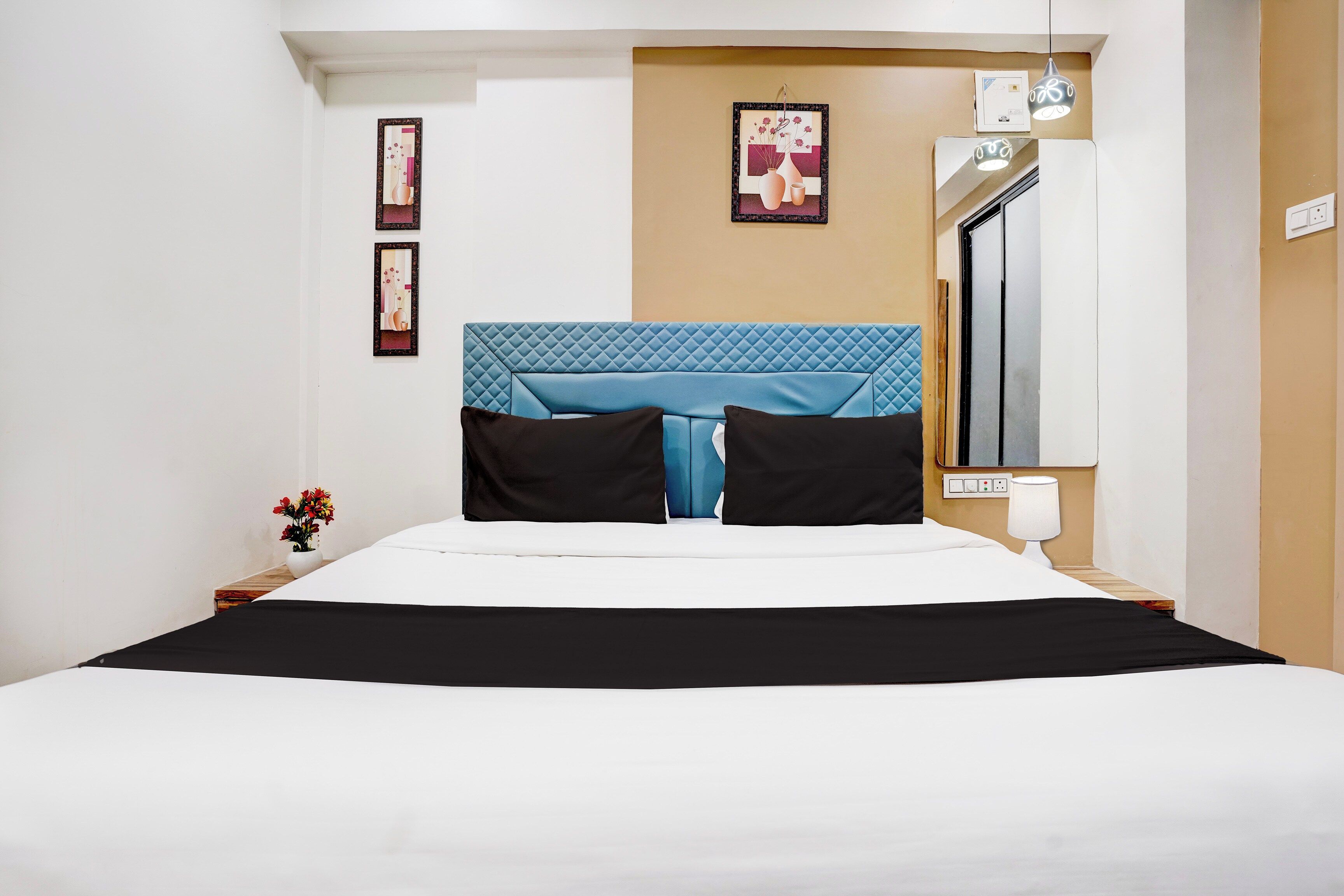 A hotel room with a bed, a nightstand, a lamp, and a wall-mounted thermostat.