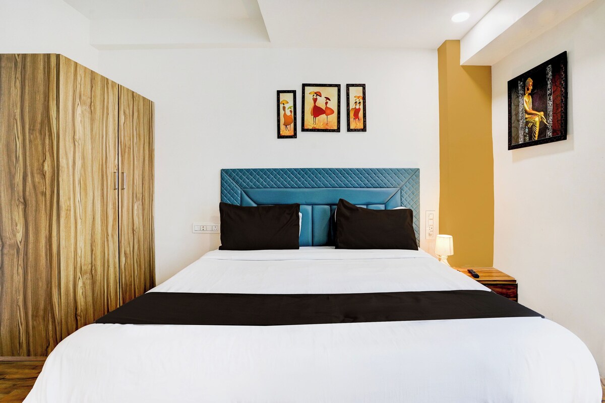 A hotel room with a bed, a wooden wardrobe, and artwork on the walls.