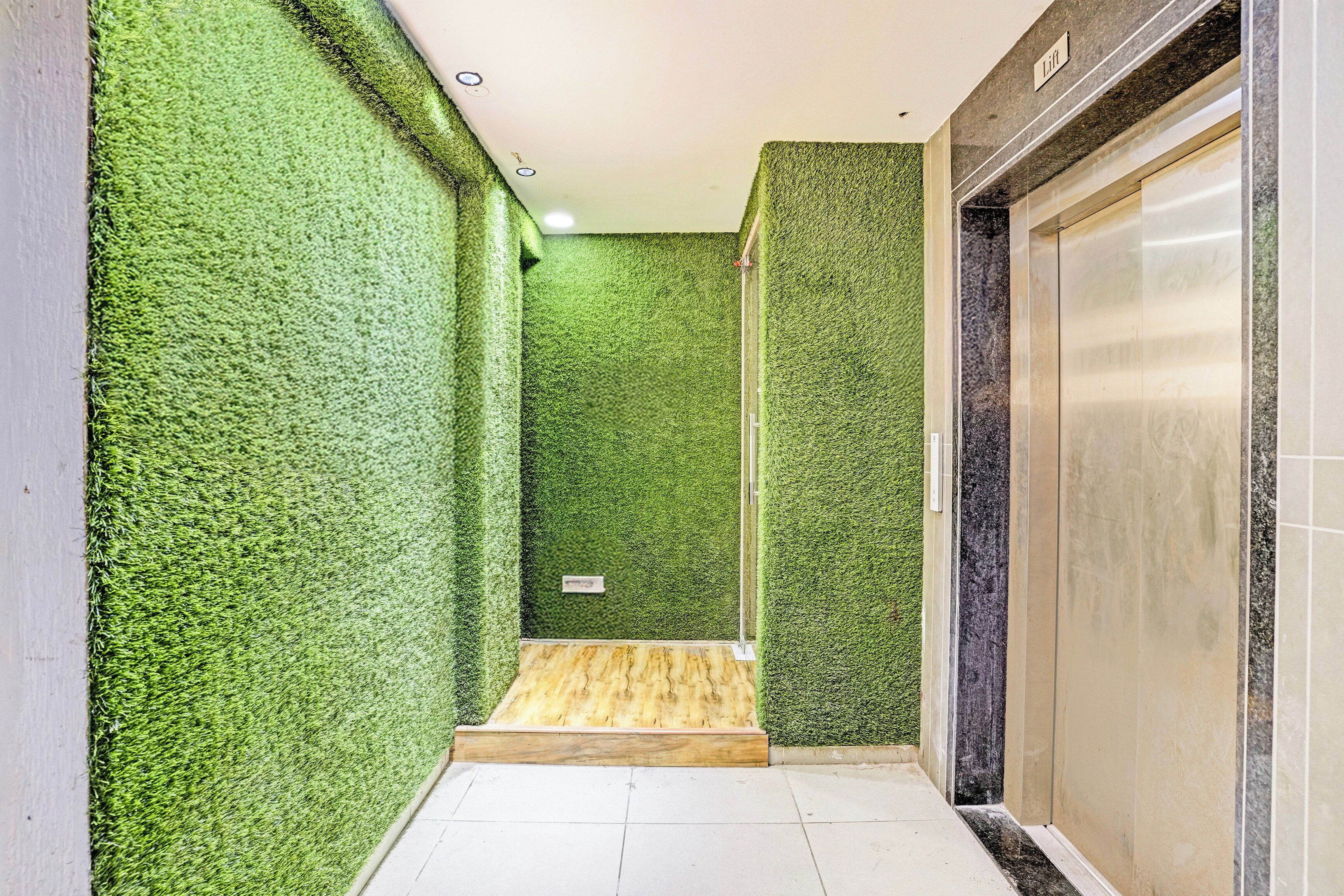 A corridor with green artificial grass walls, a wooden bench, and a closed elevator door.