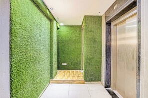 A corridor with green artificial grass walls, a wooden bench, and a closed elevator door.
