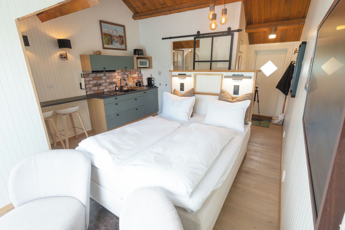 Quarto com cama grande, escrivaninha e cozinha compacta.