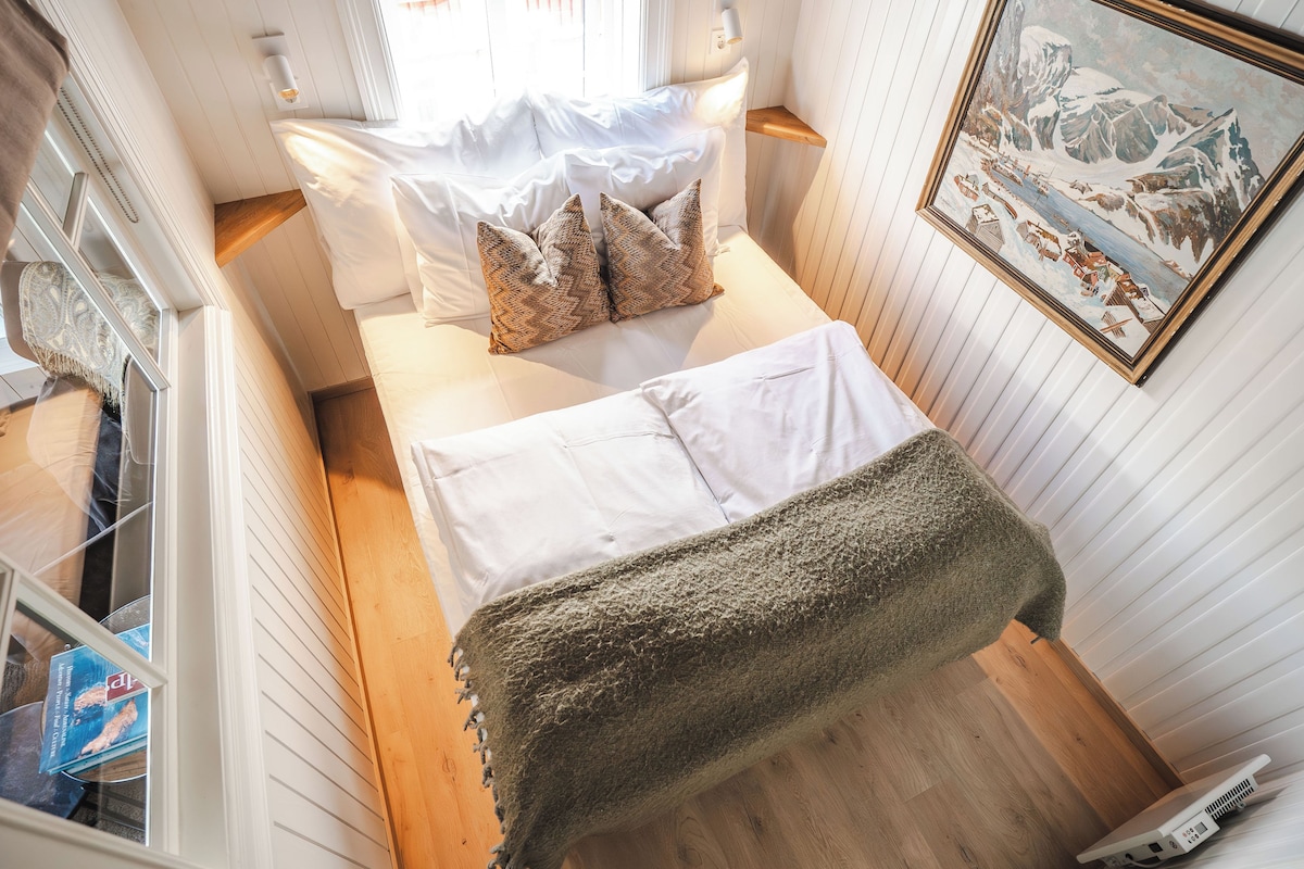 Um quarto pequeno com uma cama, piso de madeira e um quadro na parede.