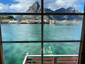 A view through a window of a coastal area with clear water, houses, and mountains.