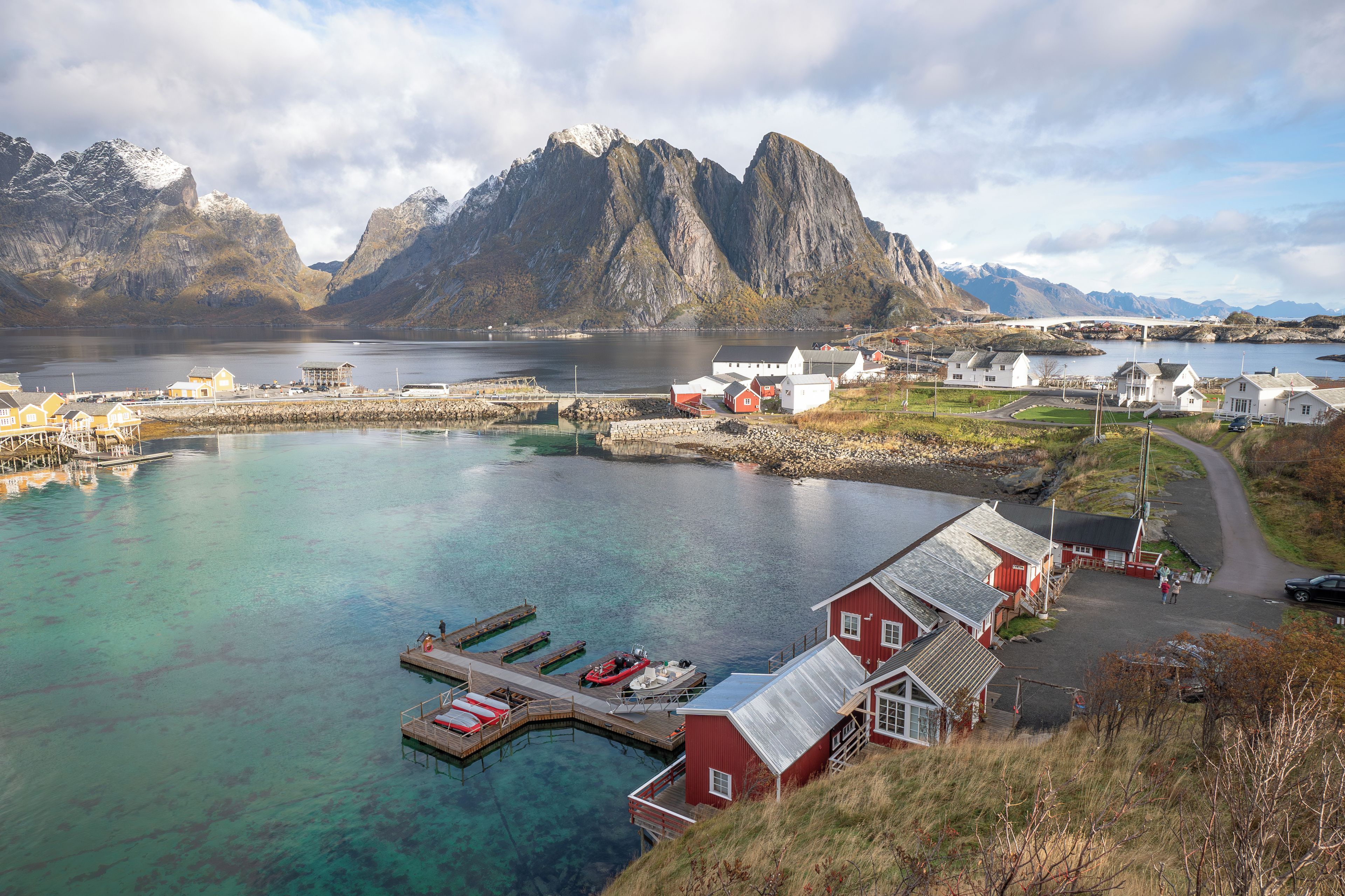 En kystlandsby med en havn, klart vand og et markant bjerg i baggrunden.