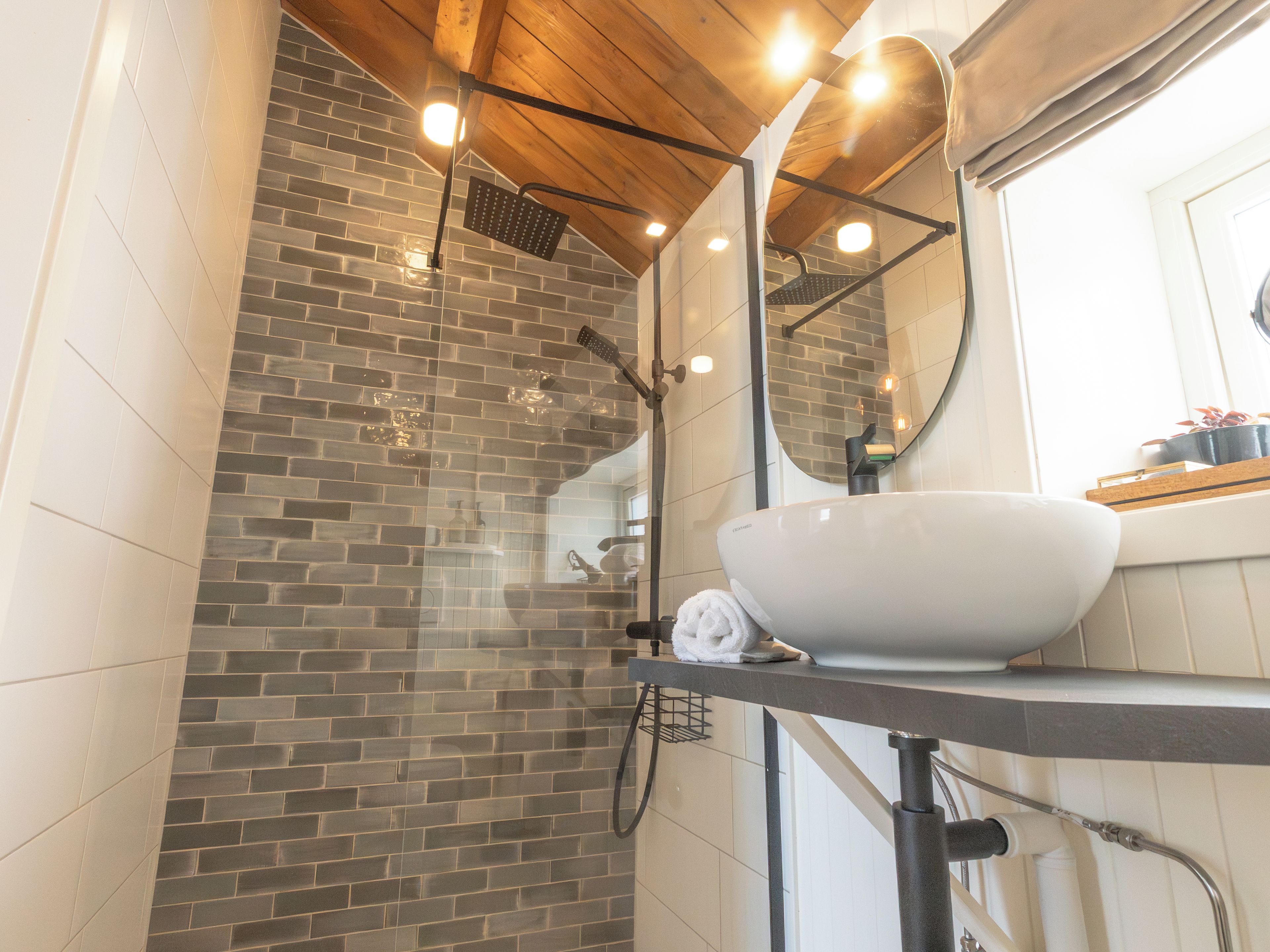 Une salle de bain avec un lavabo blanc, un miroir et une douche dotée d’un plafond en bois.