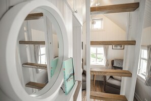 Una habitación con un espejo circular grande, estanterías de madera, un sofá y una ventana con cortinas.