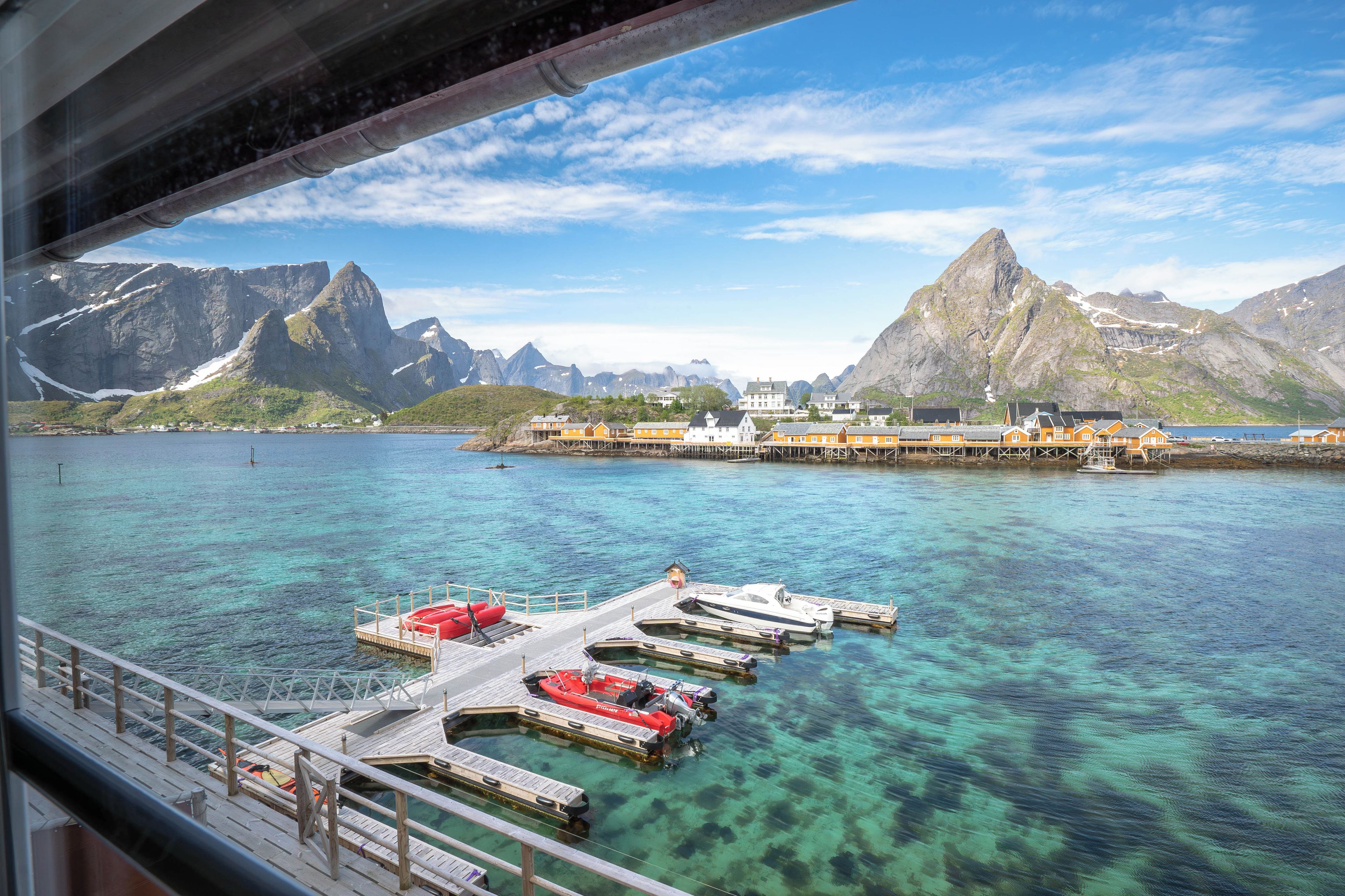 A pier with boats docked, clear water, and a mountainous landscape in the background.
