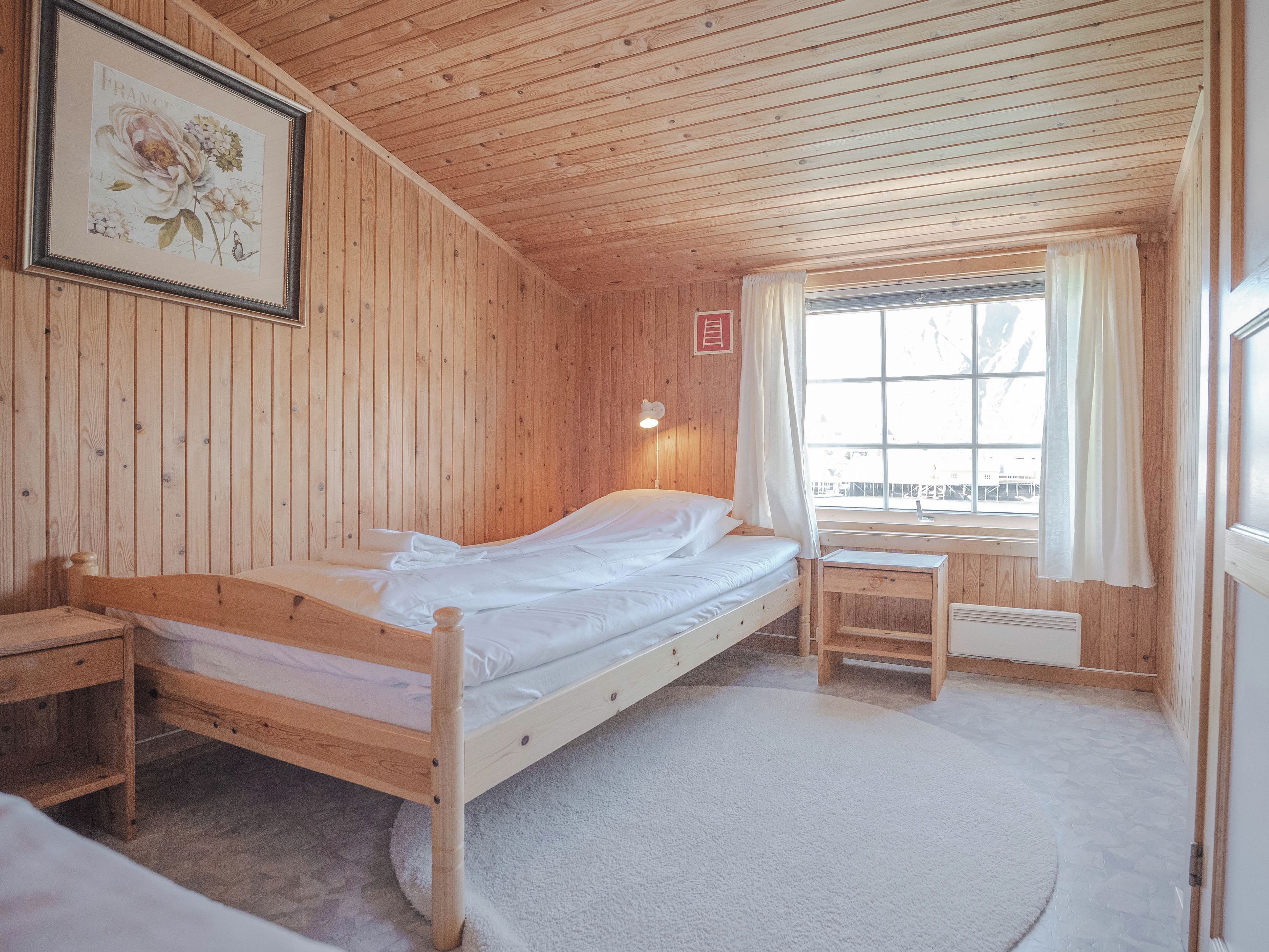 A wooden room with a bed, a desk, and a window with curtains.
