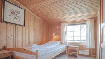 A wooden room with a bed, a desk, and a window with curtains.