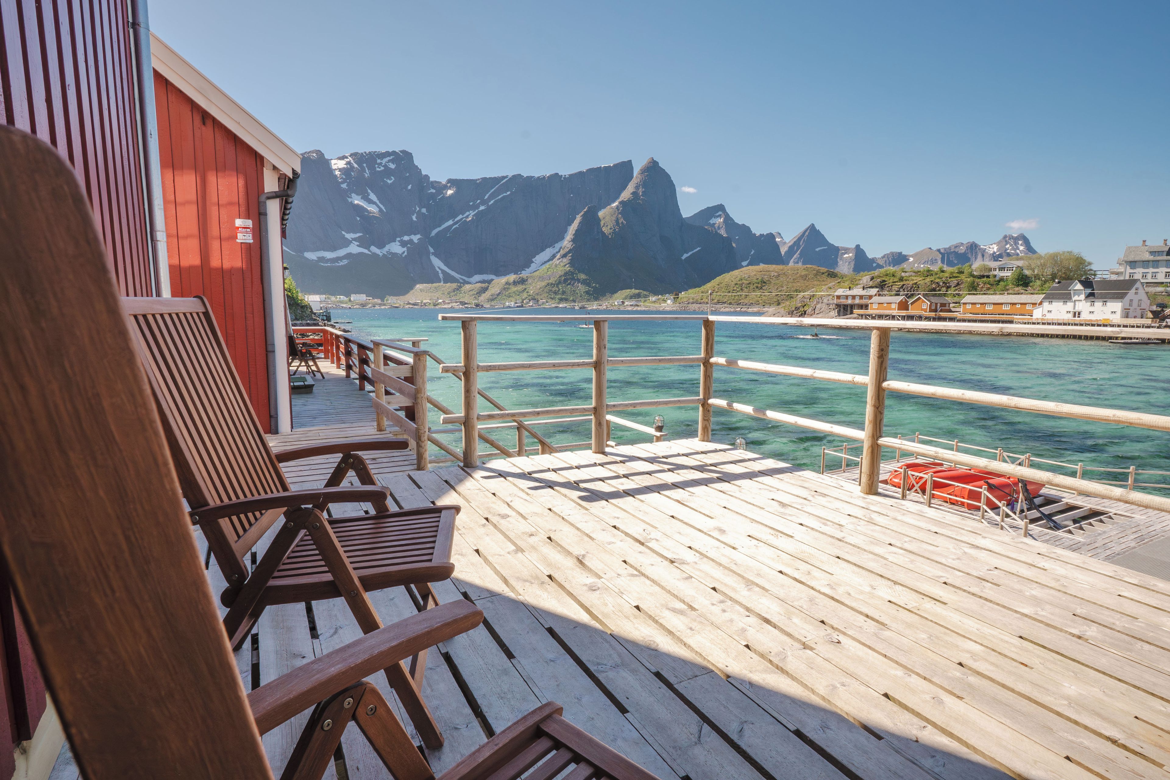 A wooden deck with chairs and a railing overlooking a body of water with mountains in the background.