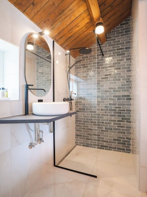 Casa de banho moderna com lavatório branco, espelho grande e chuveiro com porta de vidro.
