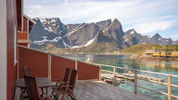 A wooden deck with chairs and a table overlooking a fjord with mountains in the background. - Rostad Retro Rorbuer (Nordland)