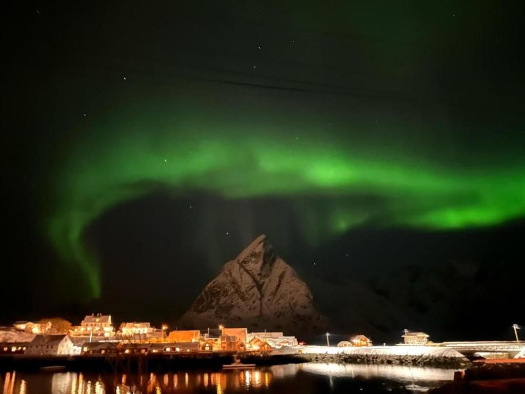 A coastal town with buildings reflecting on calm water, under a night sky with green aurora.