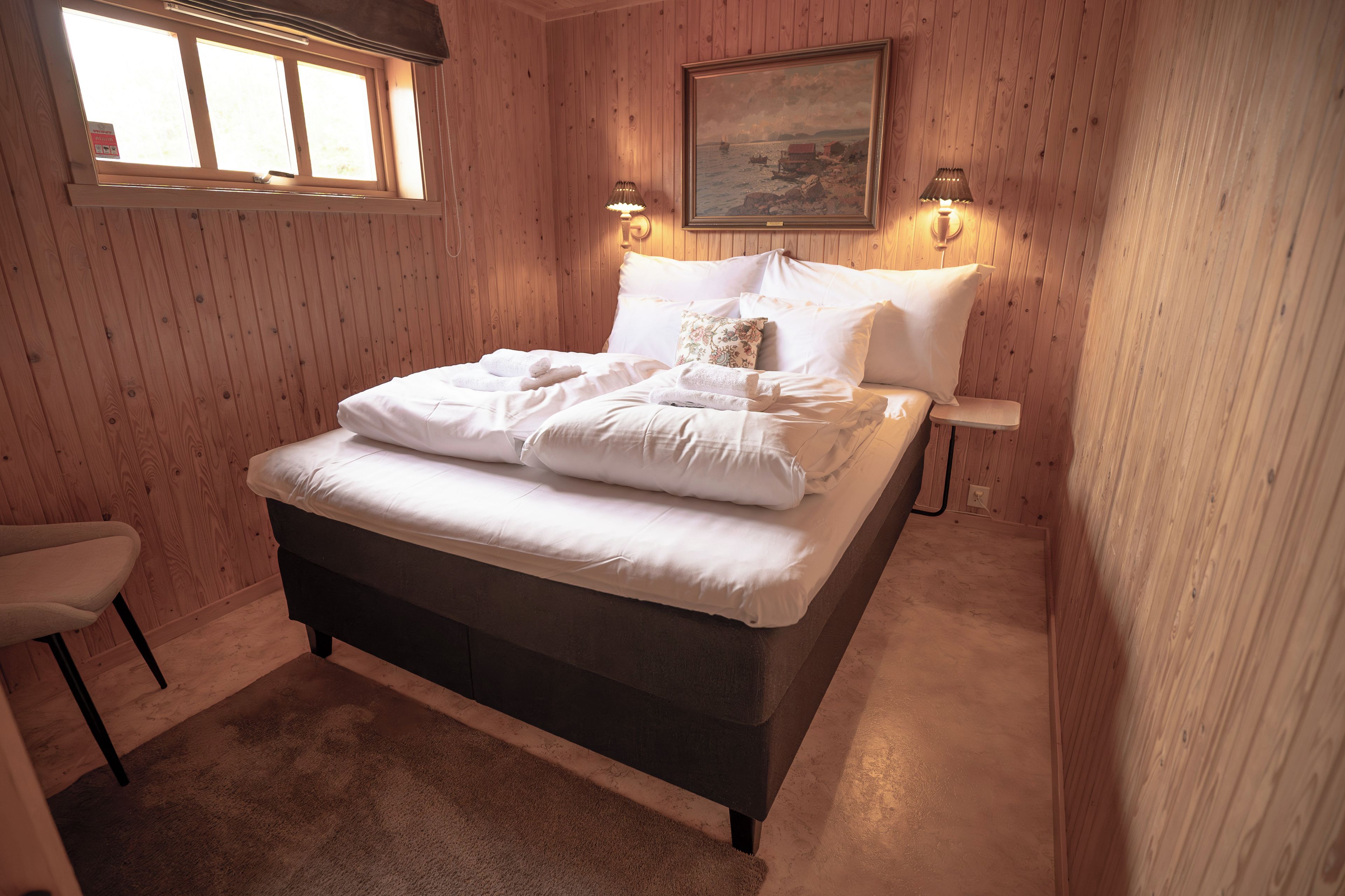 Ein Schlafzimmer mit Bett, Stuhl, einem Bild an der Wand und einem Fenster.