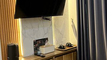 Ein Hotelzimmer mit einem an der Wand montierten Flachbildfernseher, einem Nachttisch aus Holz inklusive Fernbedienung, einer Taschentuchbox und einem kleinen dekorativen Gegenstand.