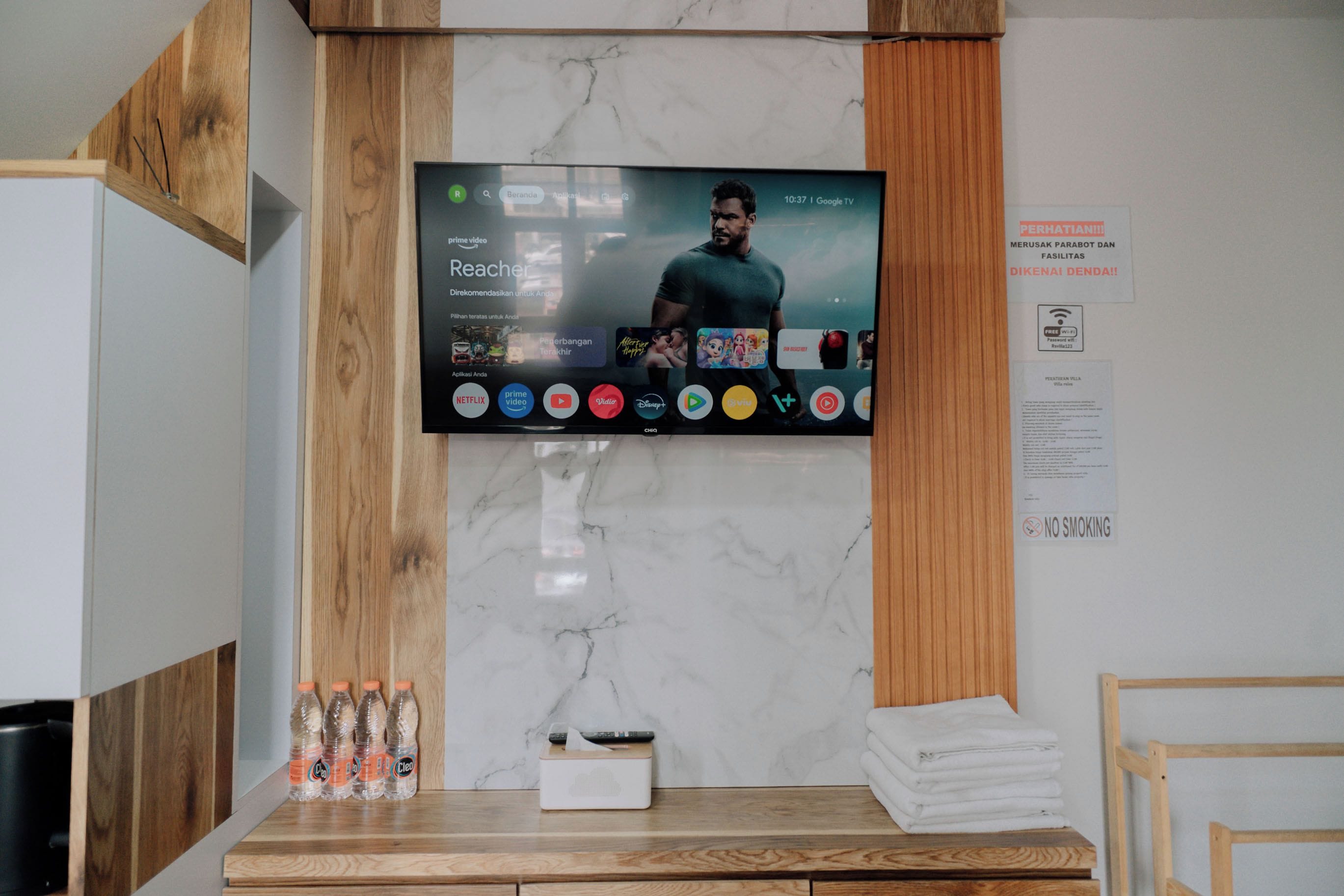 Zona de recepción de un hotel con un televisor montado que muestra diversos servicios de streaming.