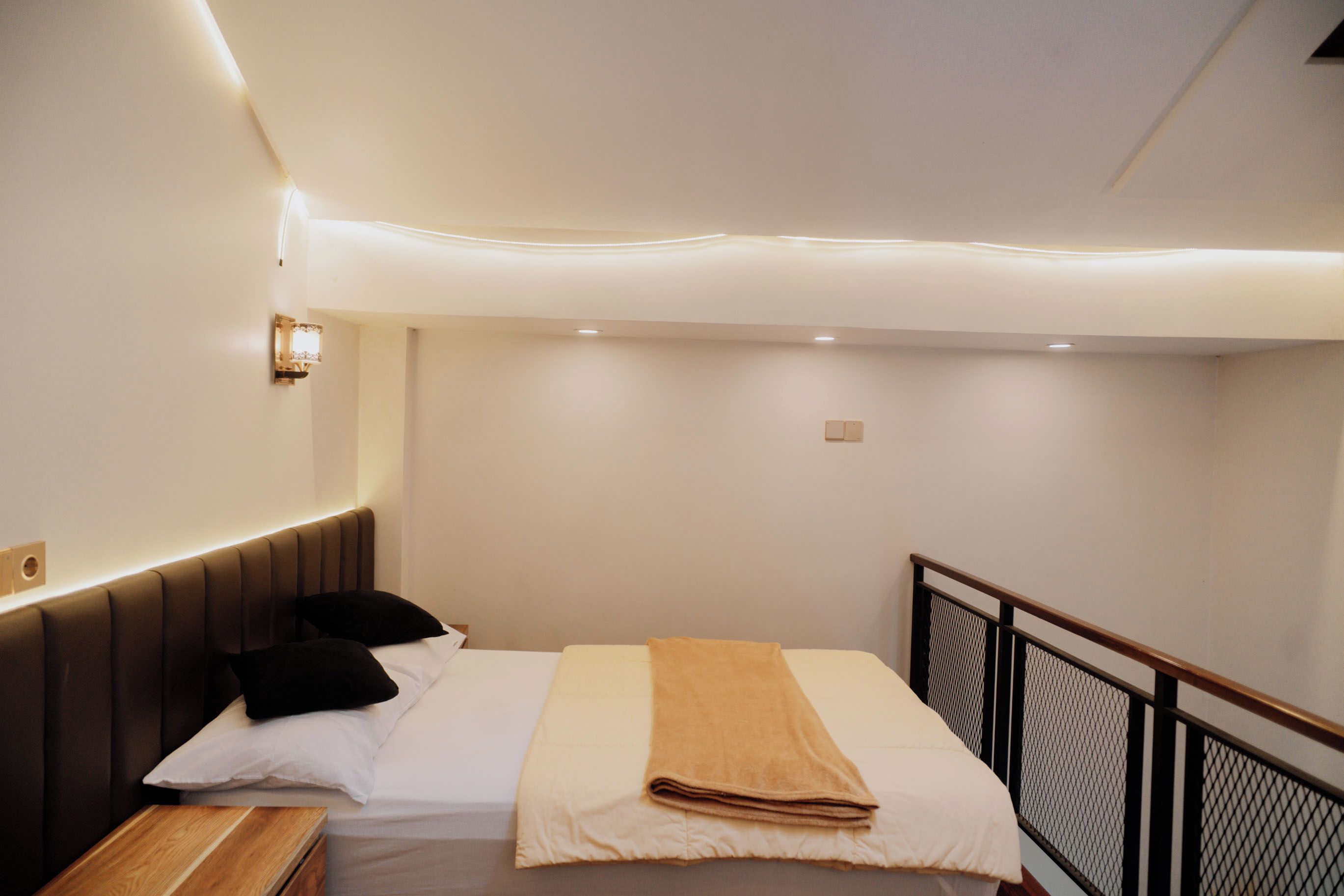 Una habitación de hotel con cama, mesita de noche y cabecera con iluminación integrada.