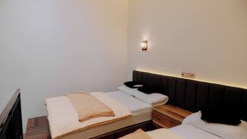 Quarto de hotel com duas camas, uma mesa de cabeceira, uma luminária na parede e piso de madeira.