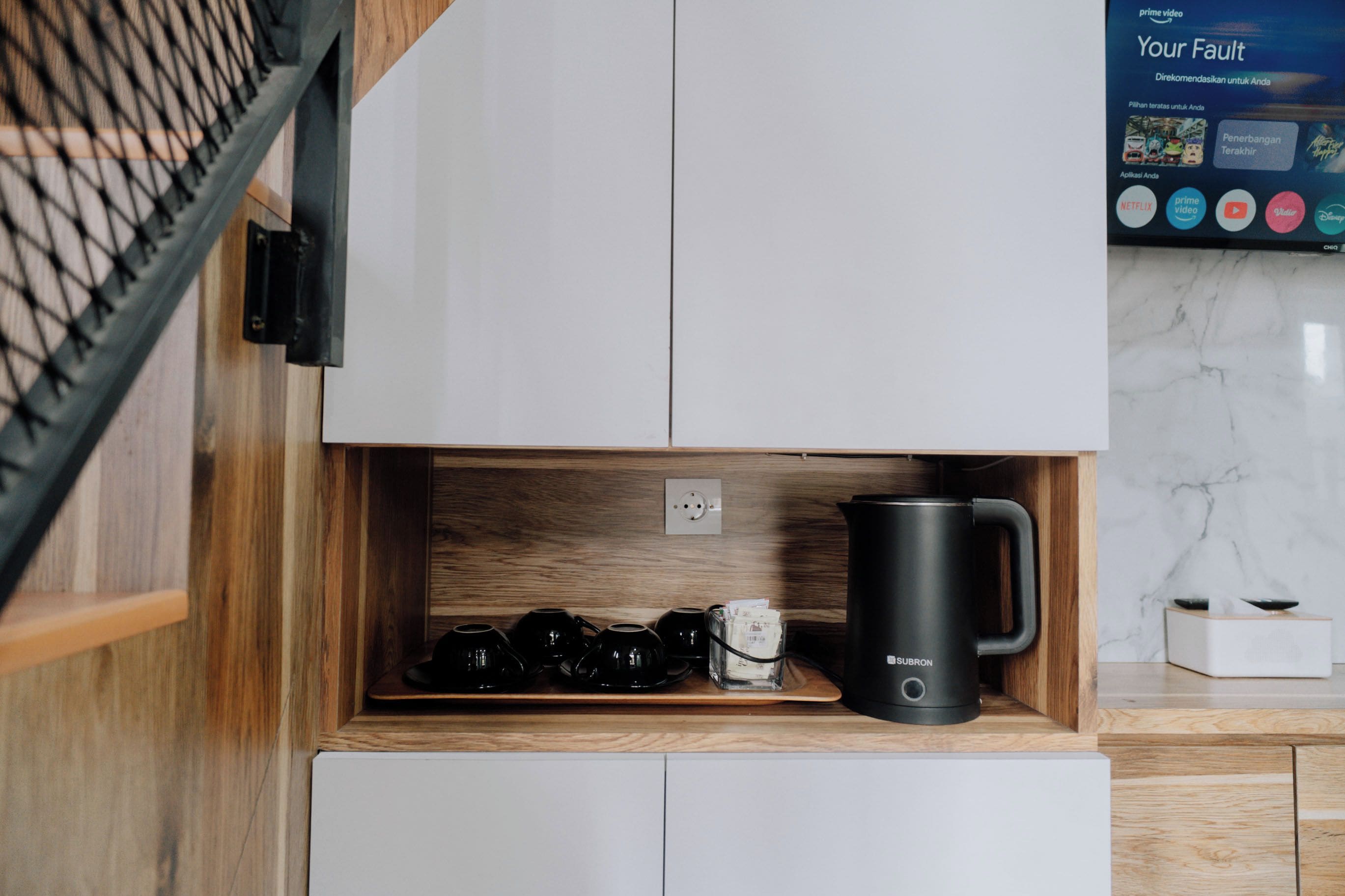 A kitchen area with a coffee machine, a kettle, and a coffee maker on a wooden shelf.