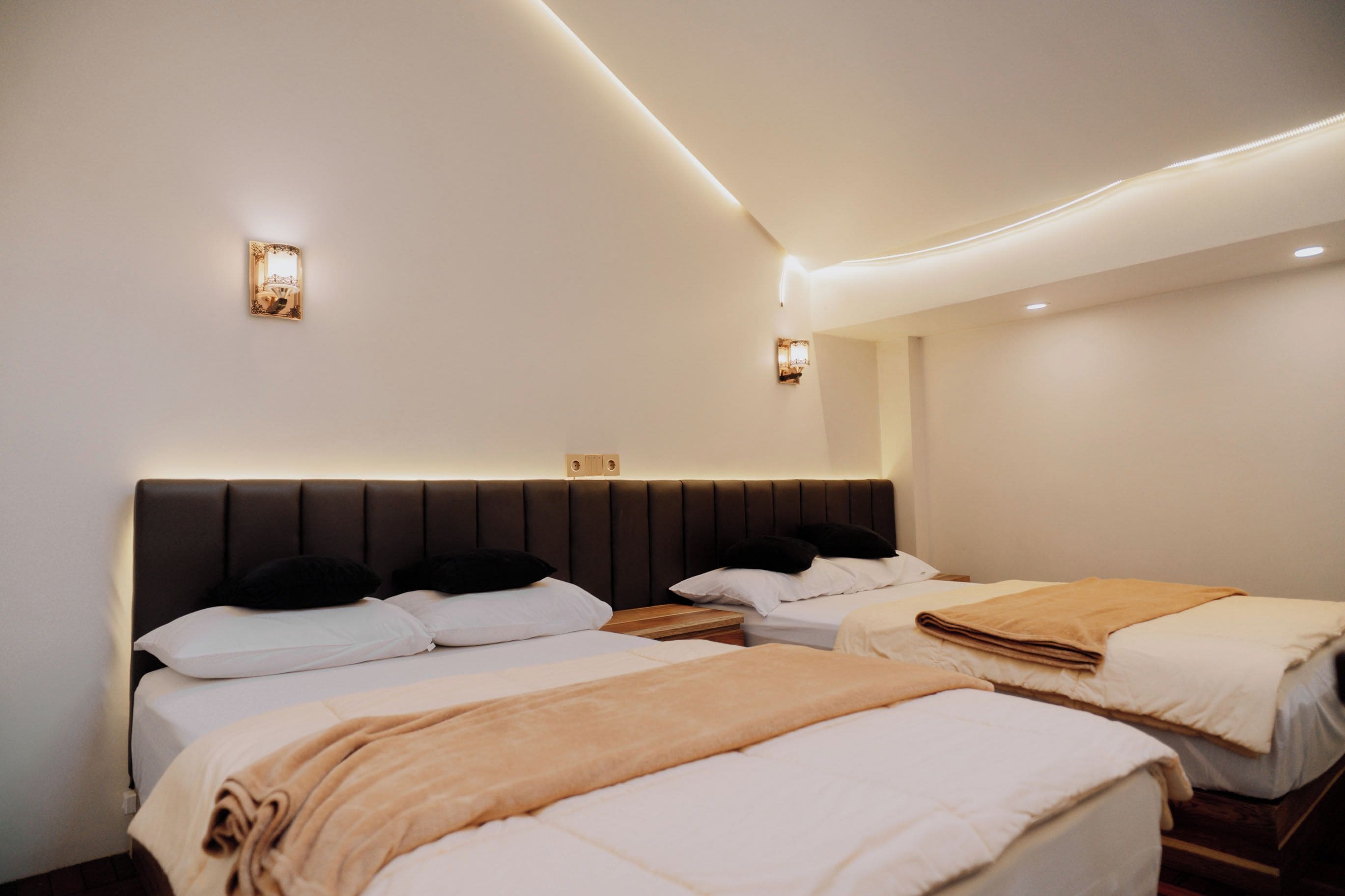 Ein Hotelzimmer mit zwei Betten, einem dunklen Kopfteil und Wandleuchten.