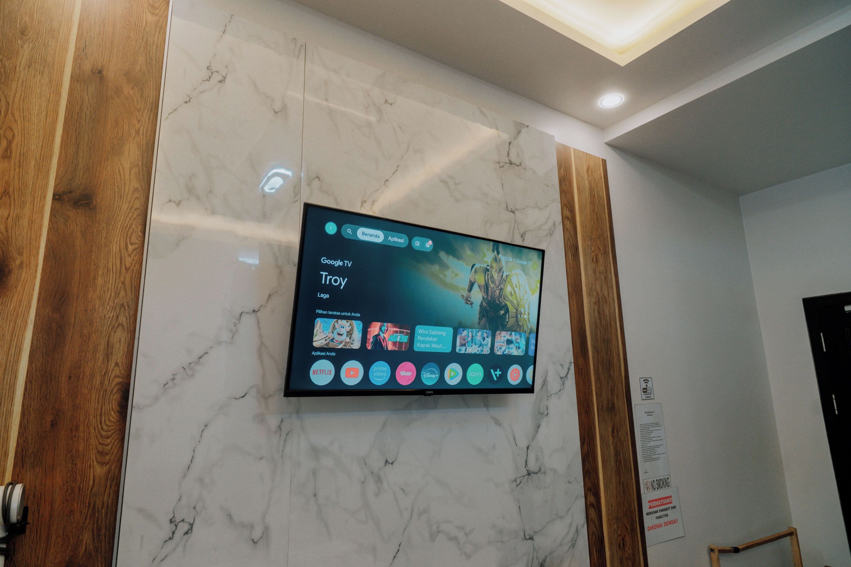 Een flatscreen televisie bevestigd aan een marmeren muur, met een Google TV interface en verschillende streaming apps.
